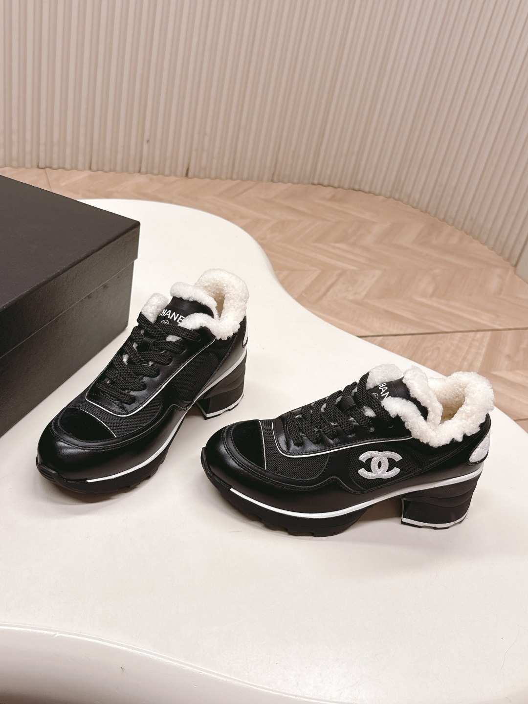 Pair of black Chanel sneakers with white shearling lining and chunky block heels on a white table - Hình 2