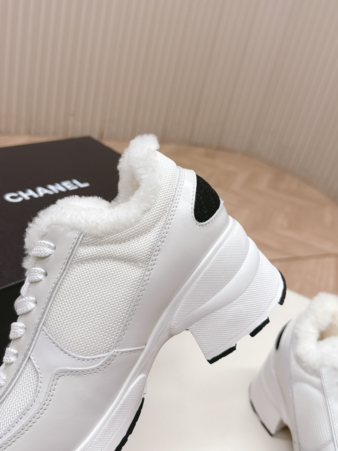 A pair of luxury Chanel white platform sneakers with plush fur lining and black toe caps displayed on a white surface. - Hình 9