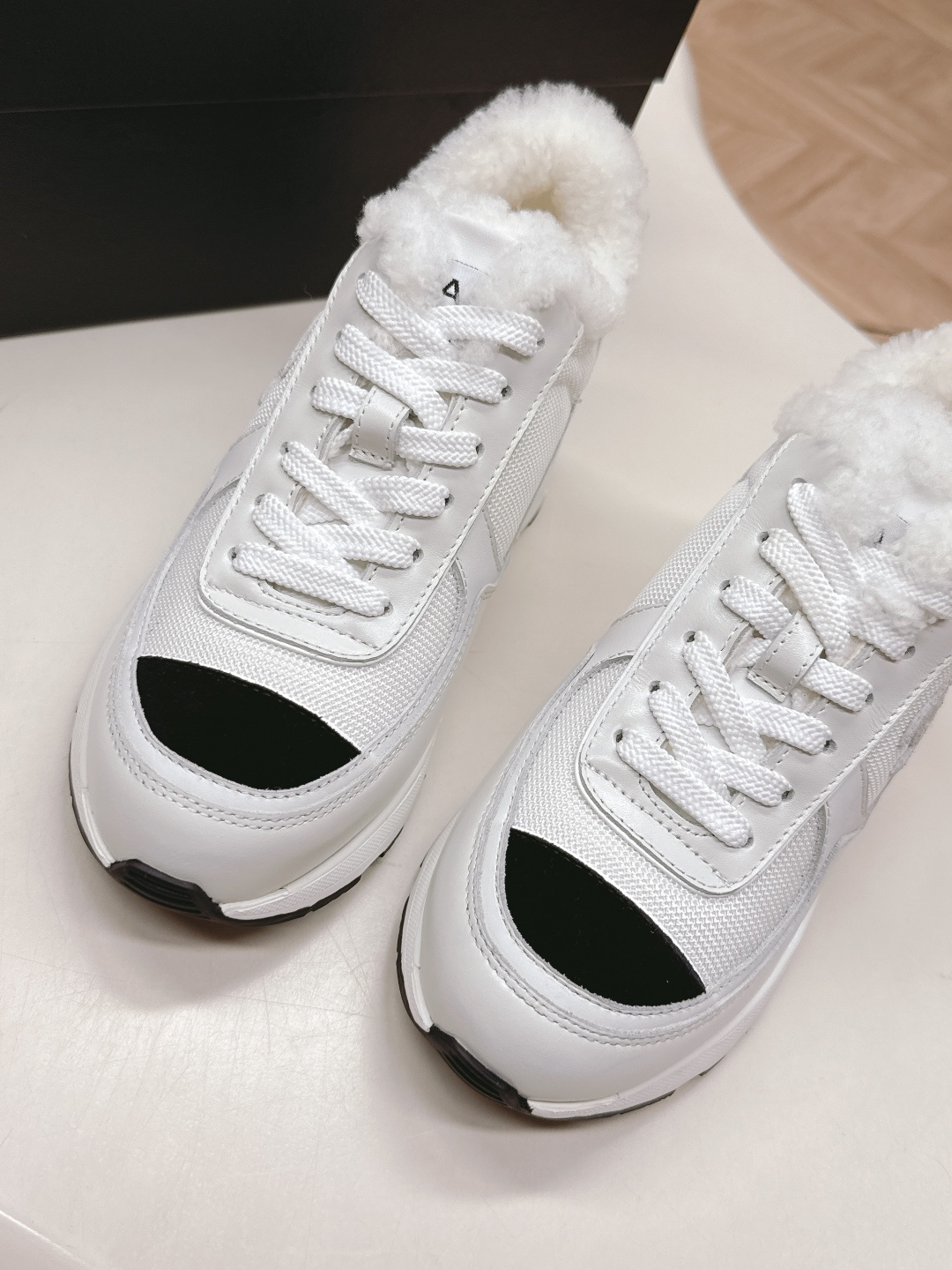 A pair of luxury Chanel white platform sneakers with plush fur lining and black toe caps displayed on a white surface. - Hình 7