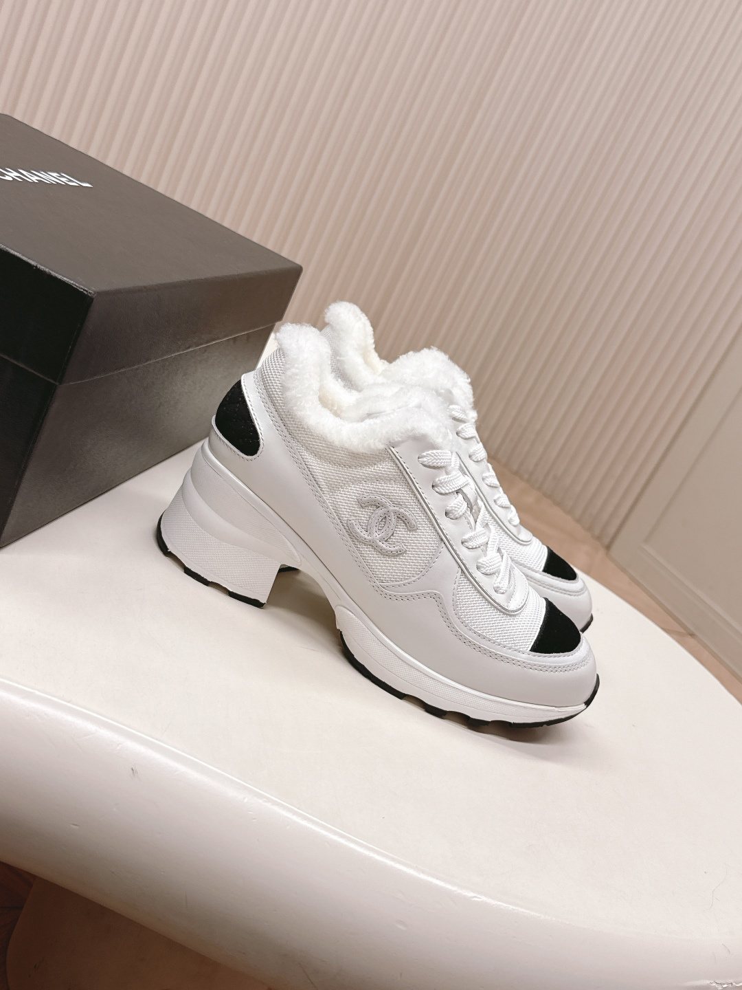 A pair of luxury Chanel white platform sneakers with plush fur lining and black toe caps displayed on a white surface. - Hình 2
