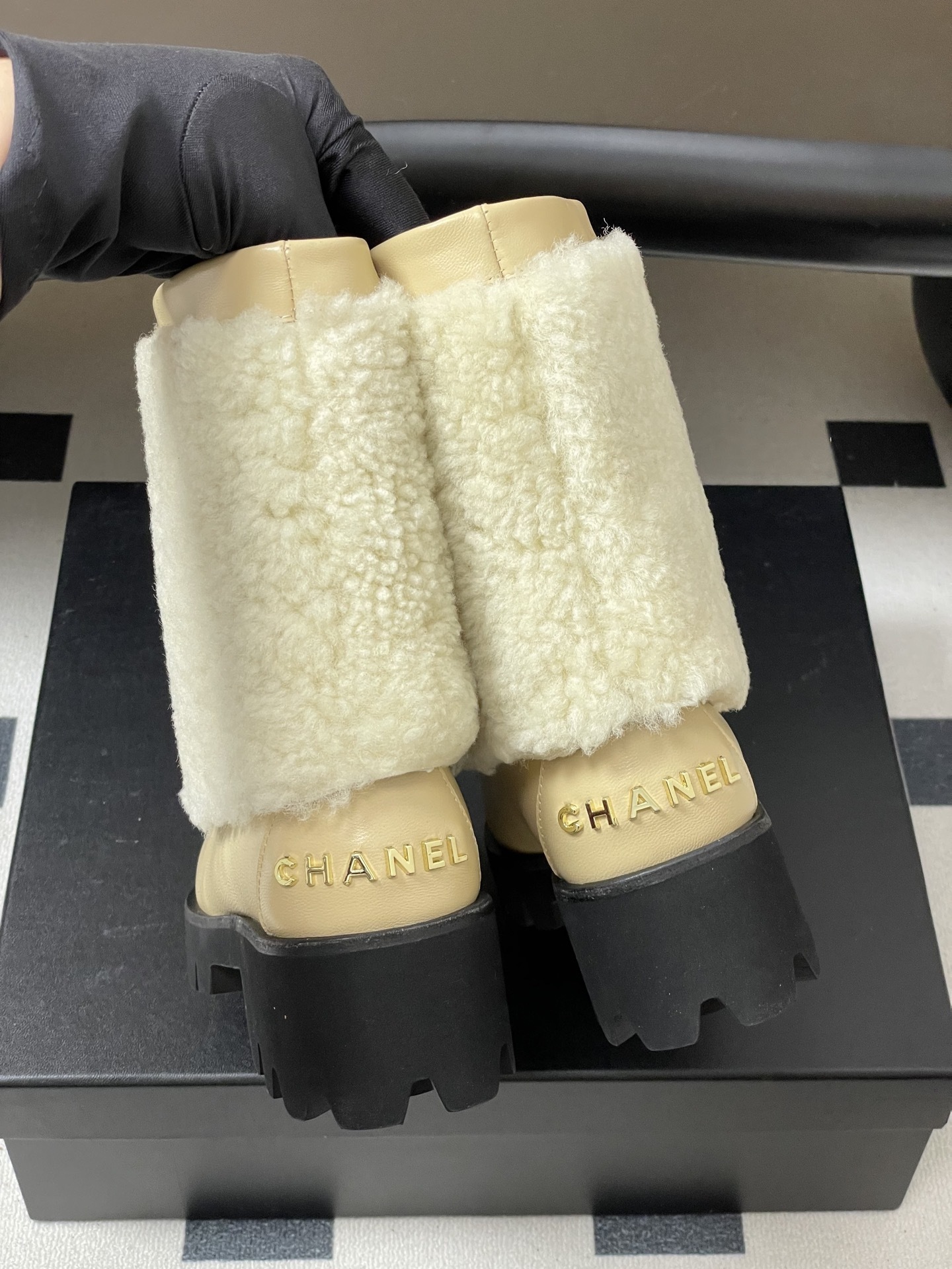 Pair of cream Chanel shearling ankle boots with black patent toe caps and velvet bows on a black table - Hình 8