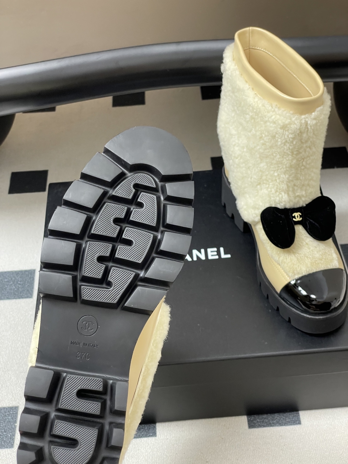 Pair of cream Chanel shearling ankle boots with black patent toe caps and velvet bows on a black table - Hình 7