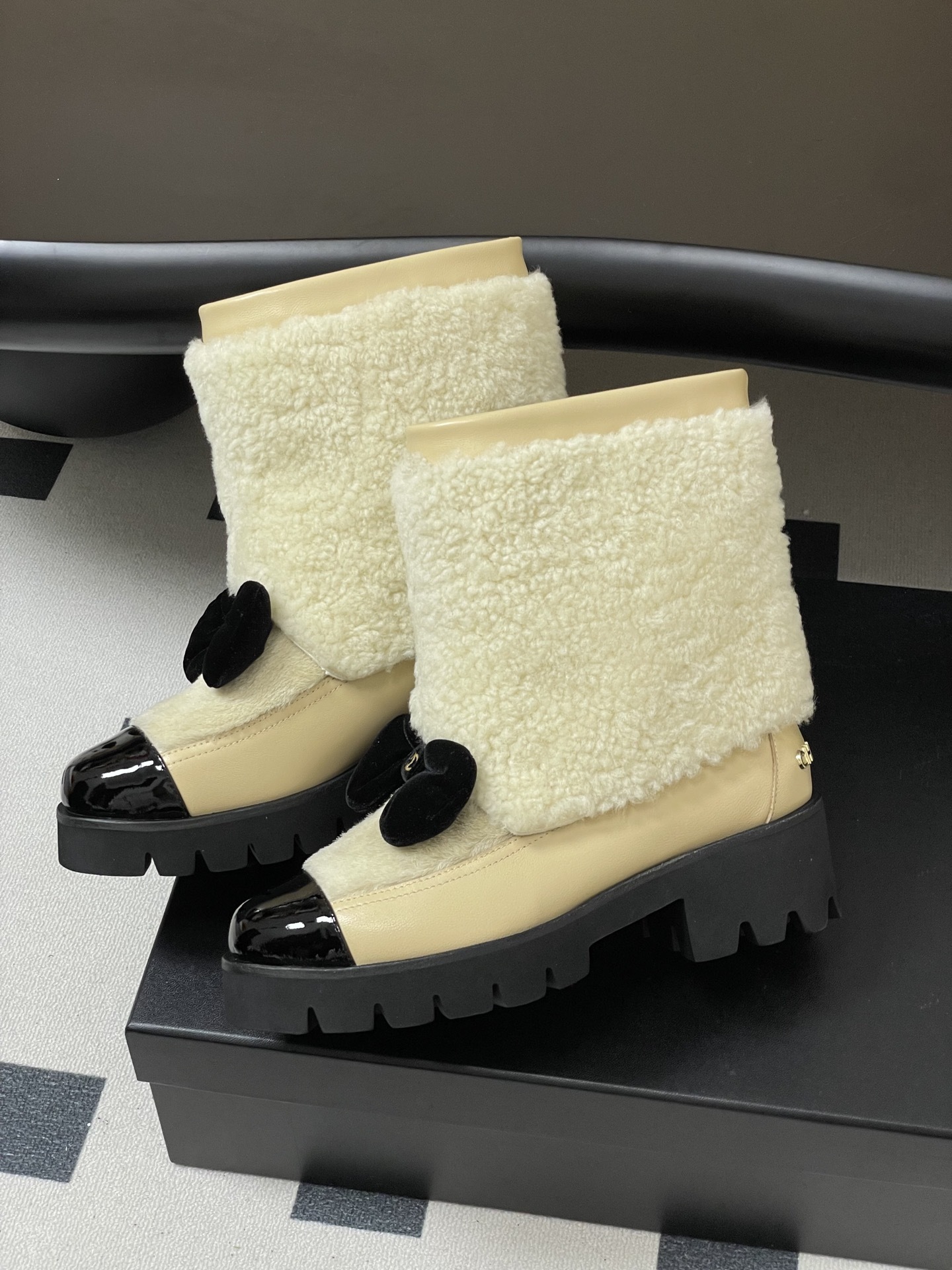 Pair of cream Chanel shearling ankle boots with black patent toe caps and velvet bows on a black table - Hình 4