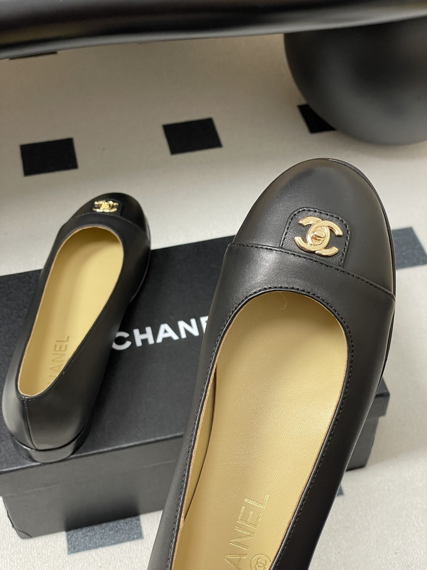 A pair of luxury Chanel black lambskin ballerina flats featuring a gold CC logo on the toe cap, displayed on a black surface. - Hình 9
