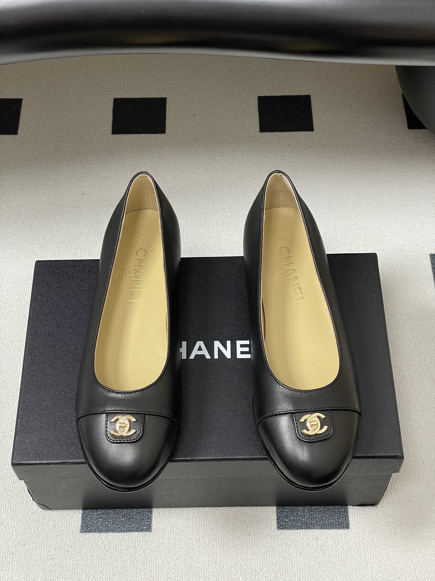 A pair of luxury Chanel black lambskin ballerina flats featuring a gold CC logo on the toe cap, displayed on a black surface. - Hình 5