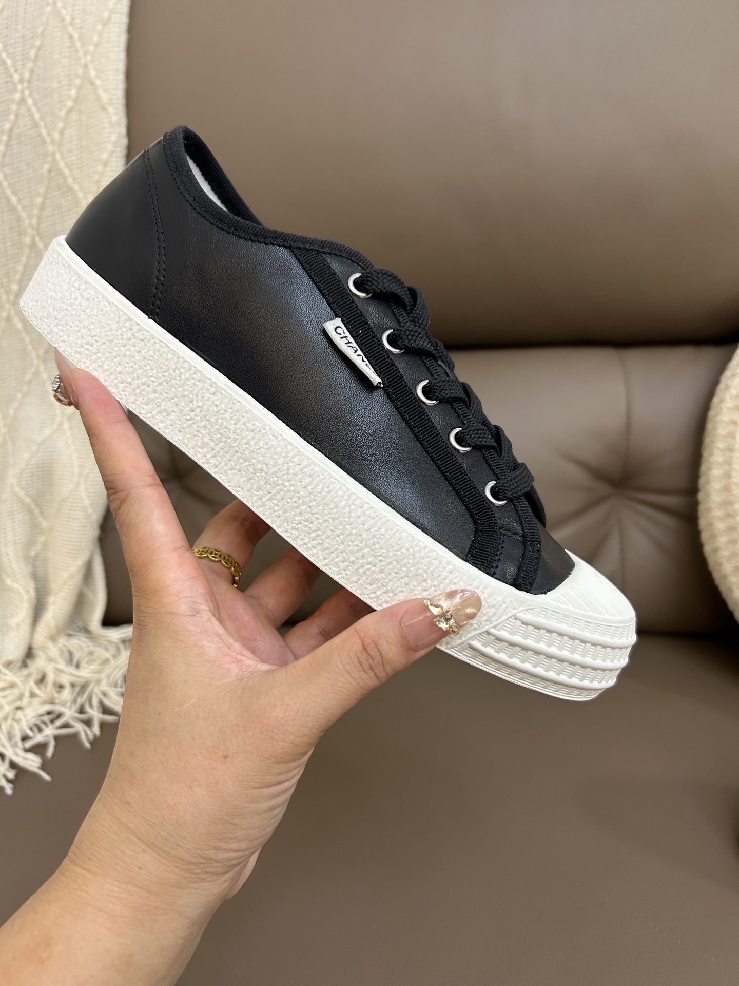Pair of Chanel luxury black leather low-top sneakers with white rubber soles and toe caps on a brown leather background. - Hình 5