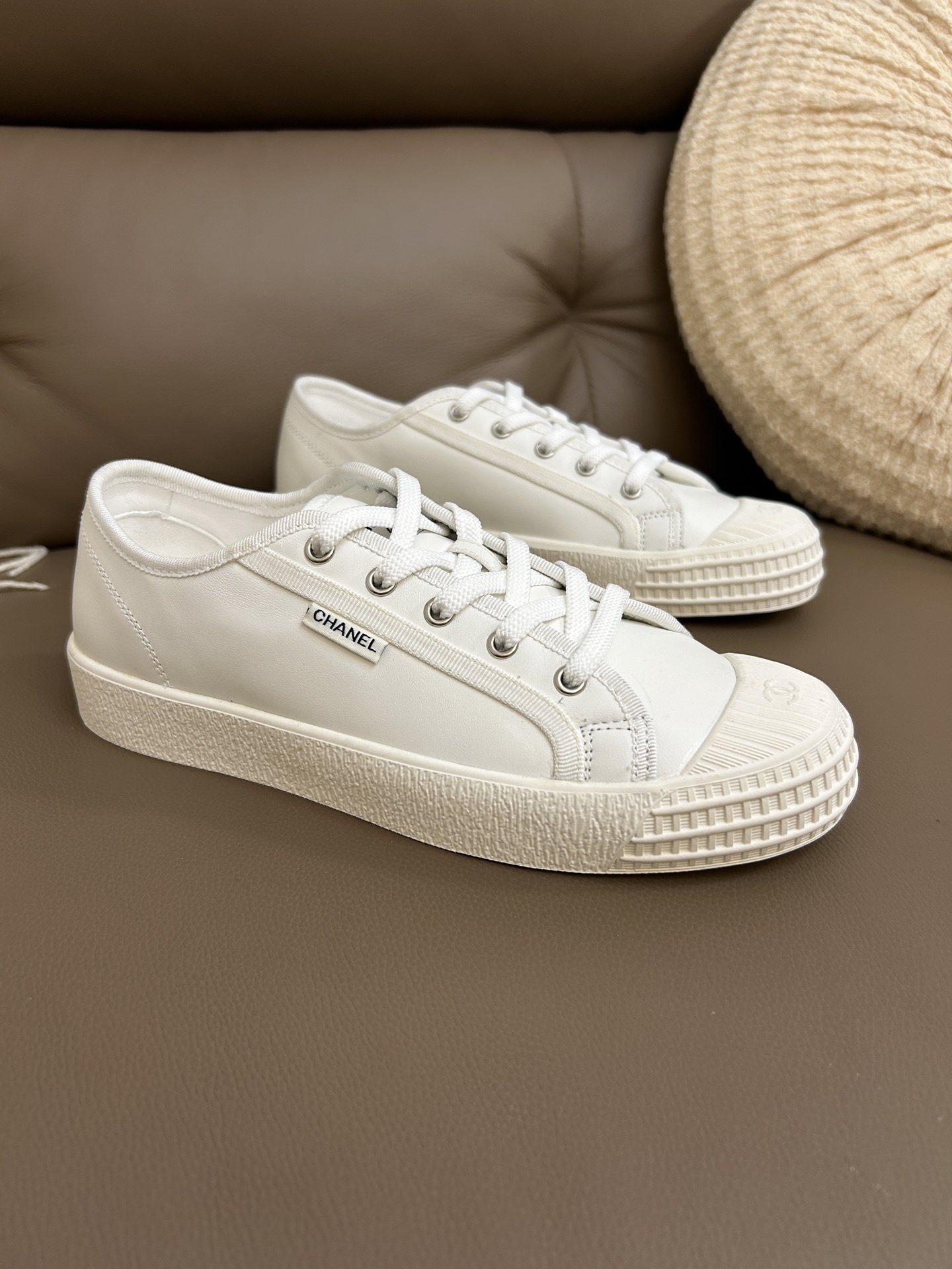 Pair of luxury Chanel white leather low-top sneakers with textured rubber toe caps featuring the CC logo. - Hình 3