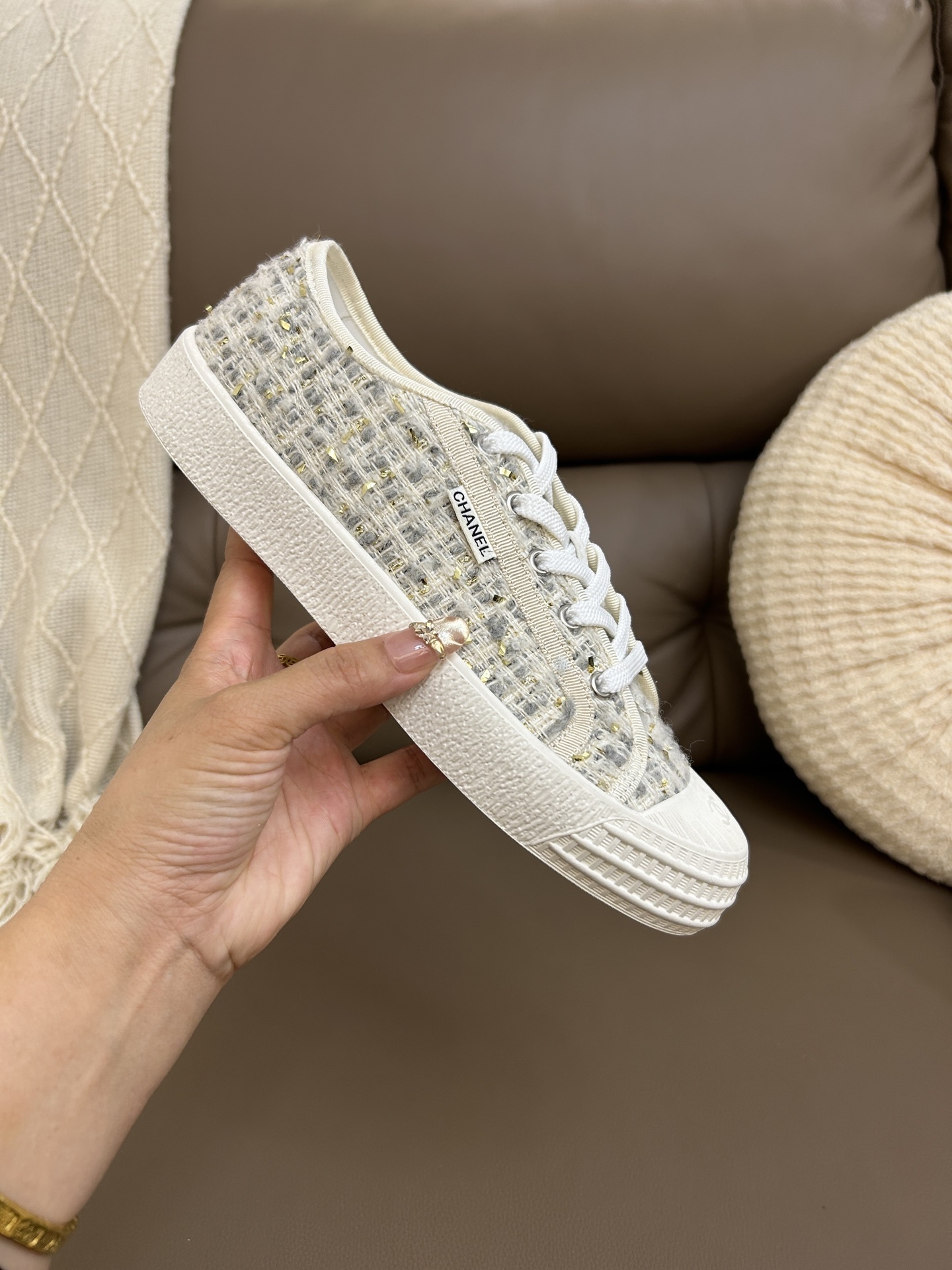 A pair of luxury Chanel low-top sneakers featuring beige and gold tweed fabric with white rubber soles and CC logo detailing. - Hình 8
