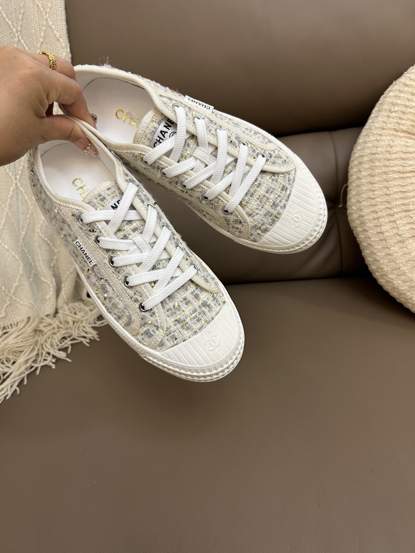 A pair of luxury Chanel low-top sneakers featuring beige and gold tweed fabric with white rubber soles and CC logo detailing. - Hình 2