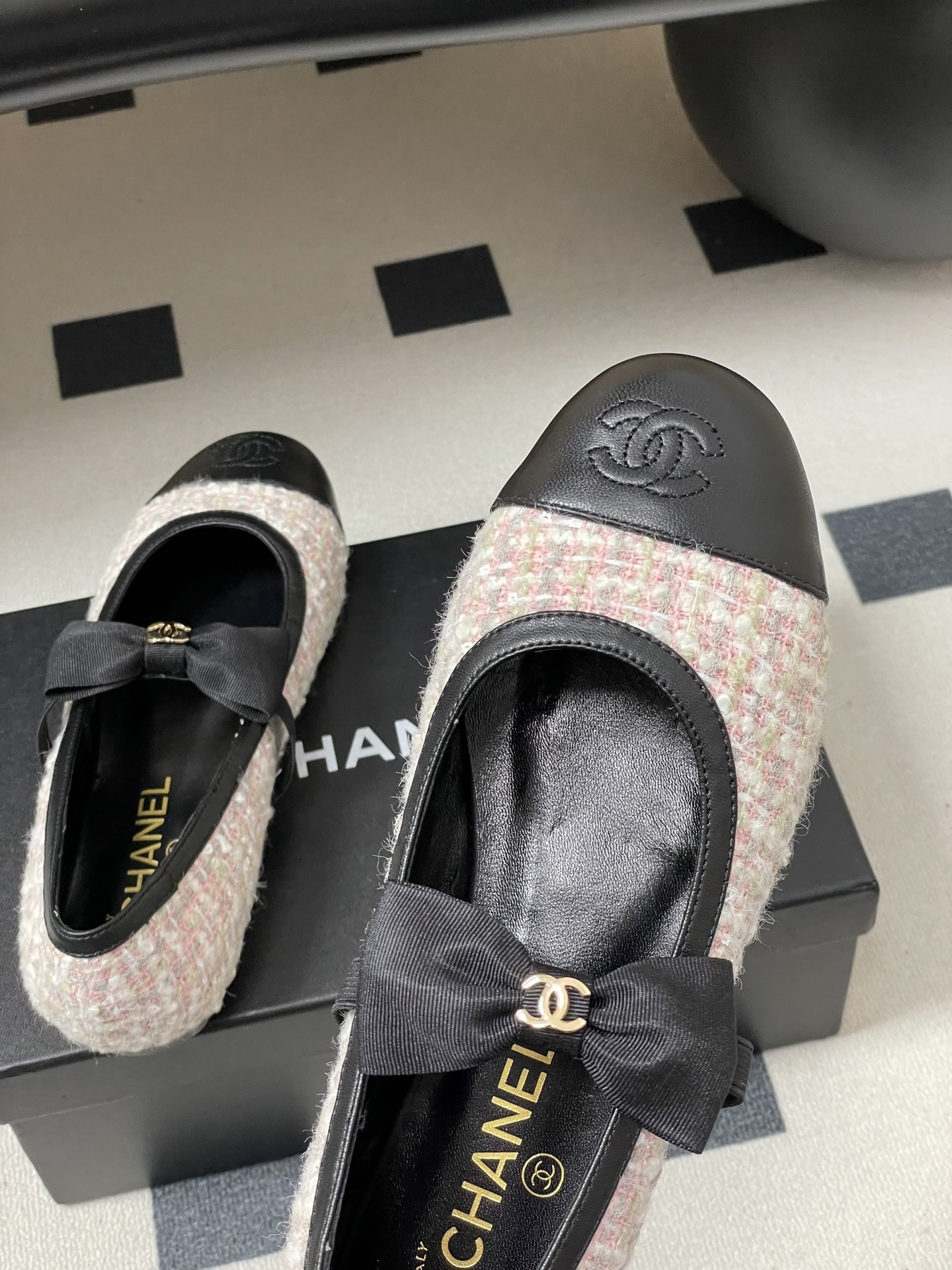 Pair of Chanel pink and white tweed ballet flats with black leather cap toes and CC logo bows on a black surface. - Hình 9