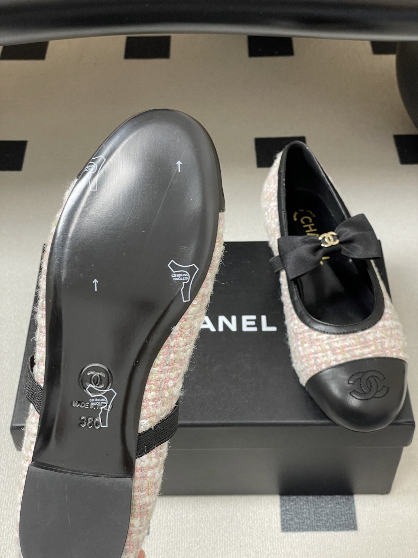 Pair of Chanel pink and white tweed ballet flats with black leather cap toes and CC logo bows on a black surface. - Hình 8