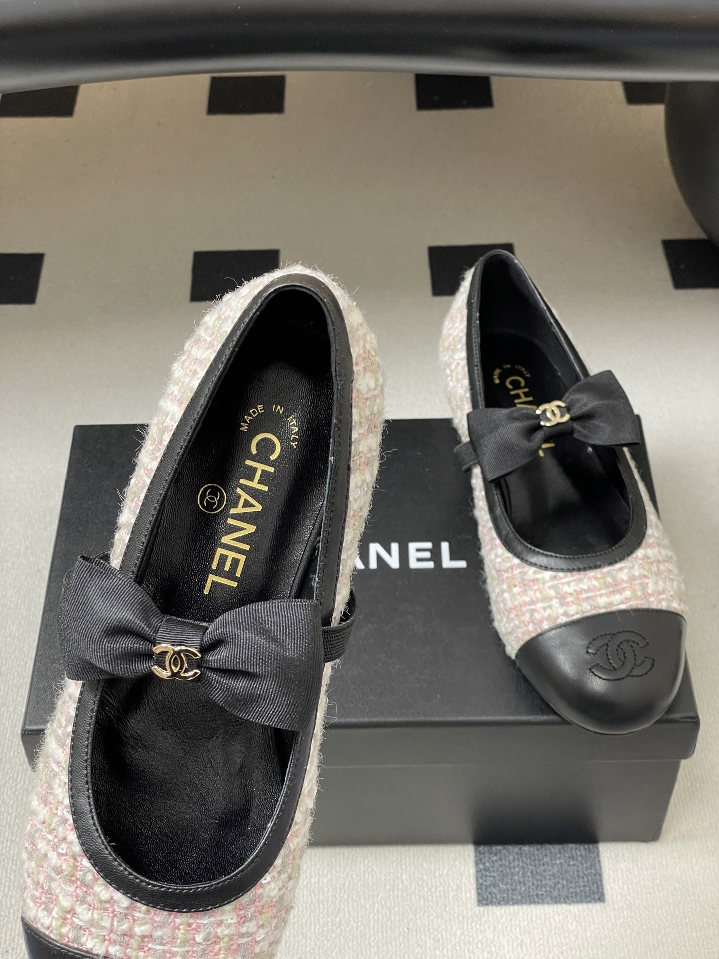 Pair of Chanel pink and white tweed ballet flats with black leather cap toes and CC logo bows on a black surface. - Hình 7