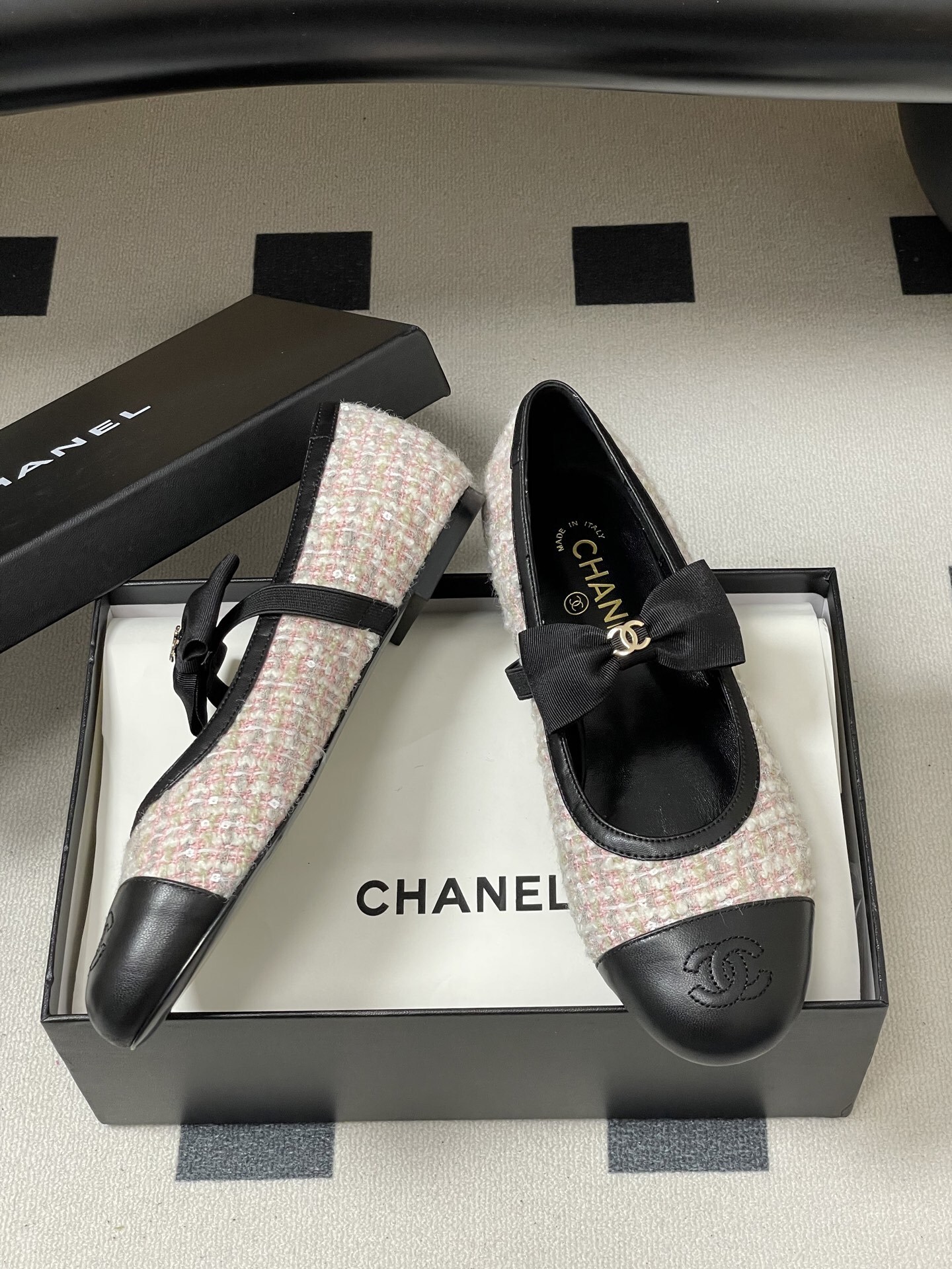 Pair of Chanel pink and white tweed ballet flats with black leather cap toes and CC logo bows on a black surface. - Hình 6