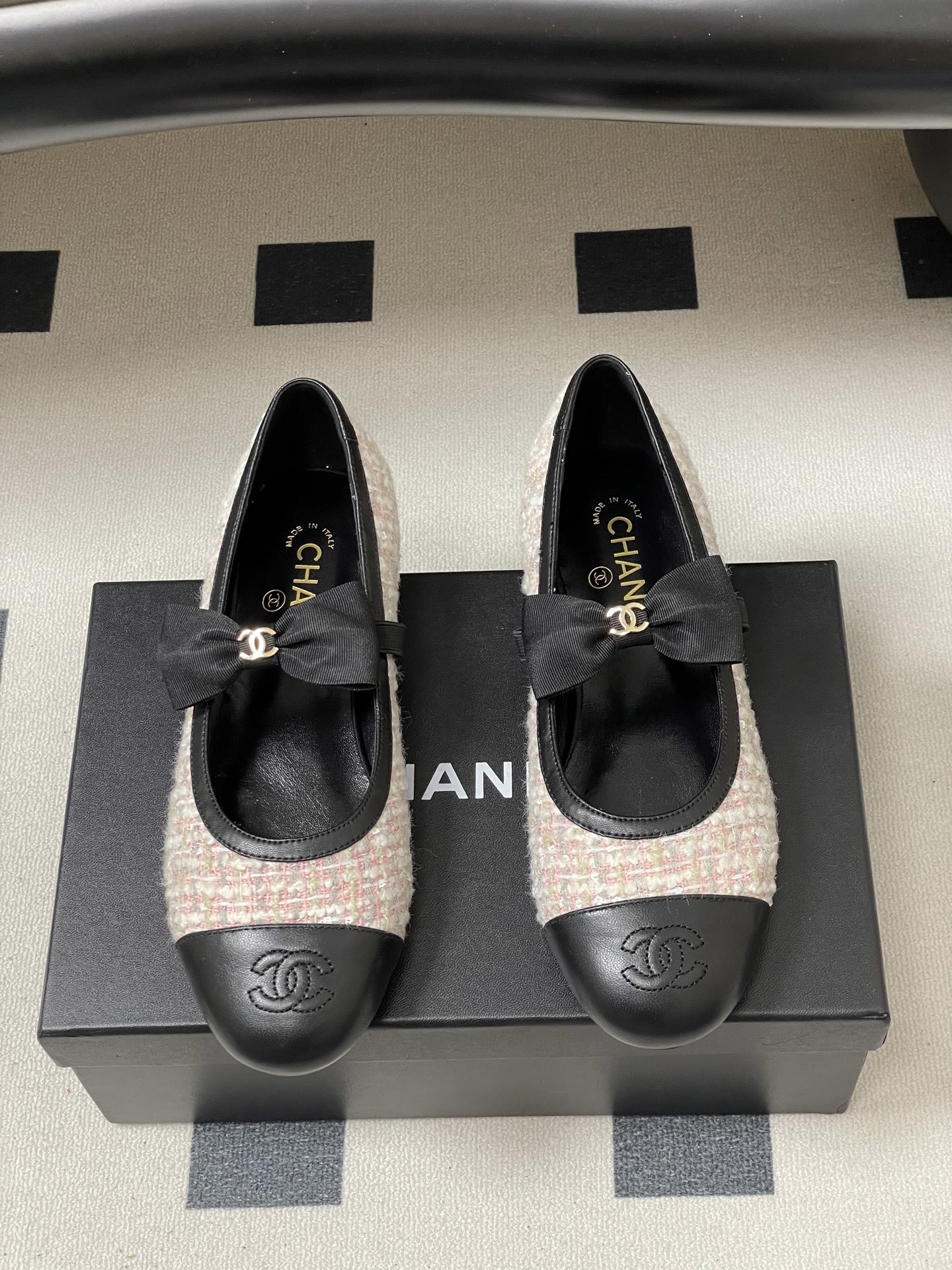 Pair of Chanel pink and white tweed ballet flats with black leather cap toes and CC logo bows on a black surface. - Hình 5
