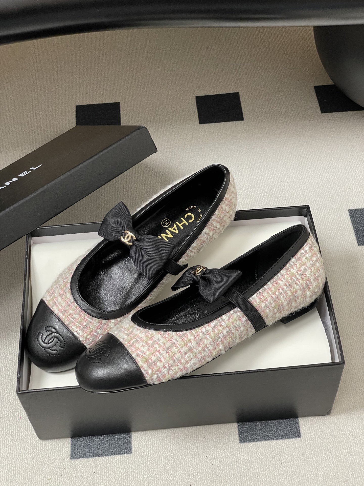 Pair of Chanel pink and white tweed ballet flats with black leather cap toes and CC logo bows on a black surface. - Hình 4