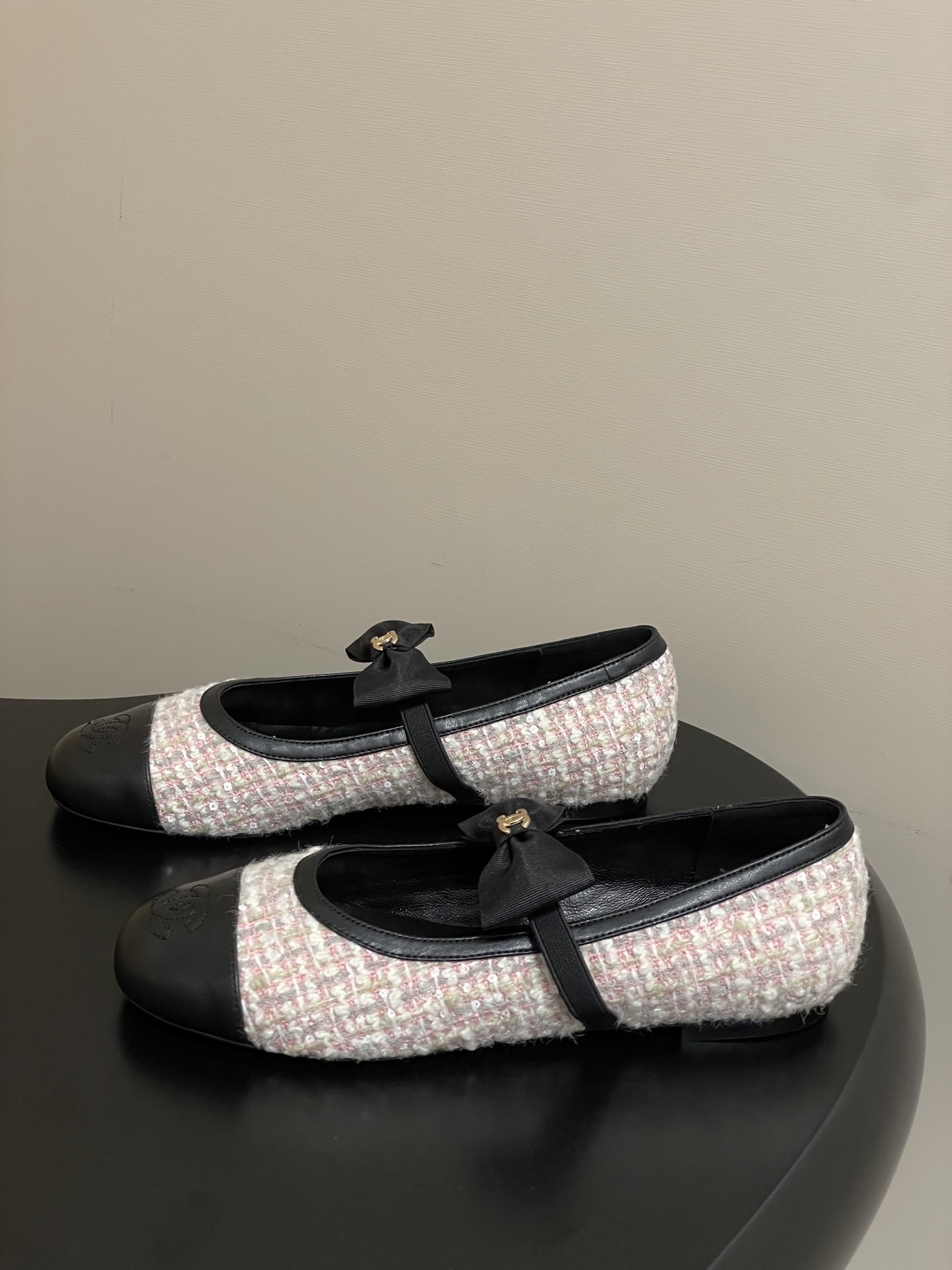 Pair of Chanel pink and white tweed ballet flats with black leather cap toes and CC logo bows on a black surface. - Hình 3