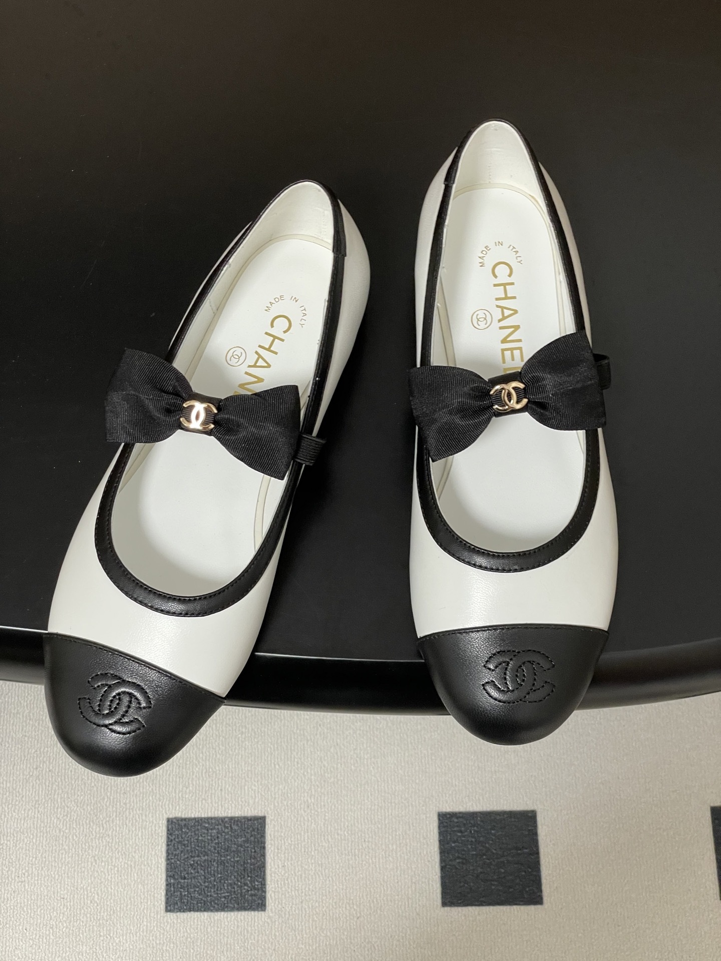 Luxury Chanel white and black leather Mary Jane flats featuring a black bow with gold logo and embroidered cap toe. - Hình 2