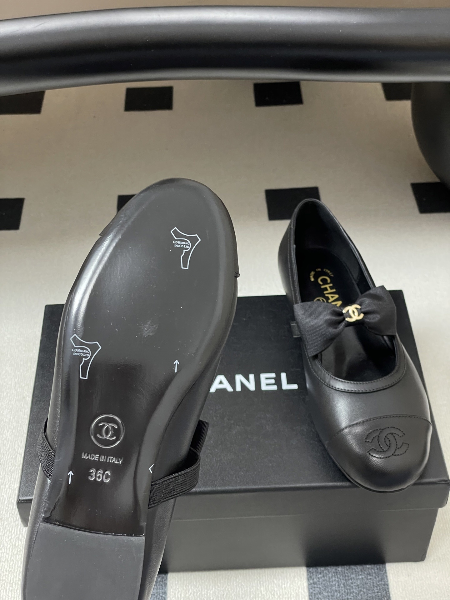 A pair of black Chanel leather ballerina flats featuring a grosgrain bow and gold-tone CC charm on a black table. - Hình 8