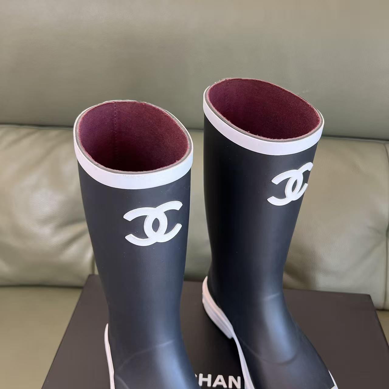 Pair of black Chanel rubber rain boots with white toe caps and interlocking CC logo on a black box - Hình 4