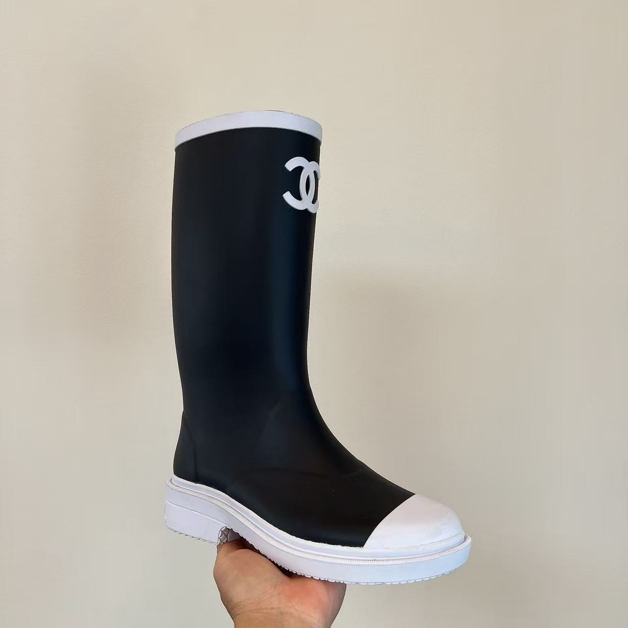 Pair of black Chanel rubber rain boots with white toe caps and interlocking CC logo on a black box - Hình 3