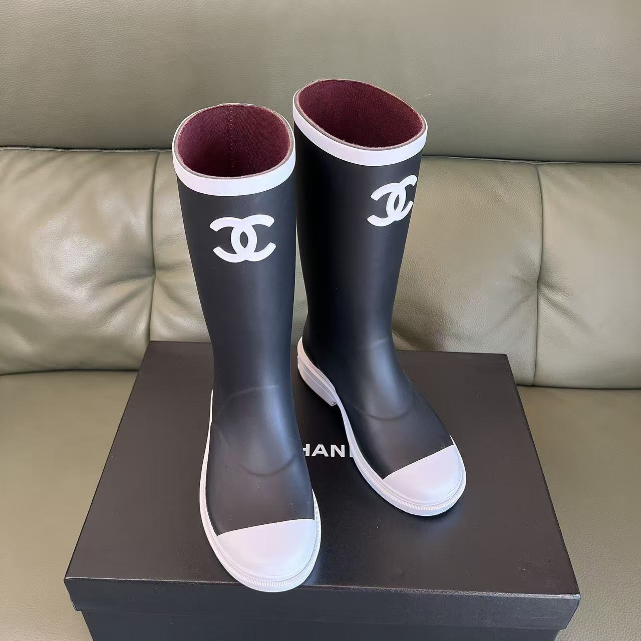Pair of black Chanel rubber rain boots with white toe caps and interlocking CC logo on a black box - Hình 2