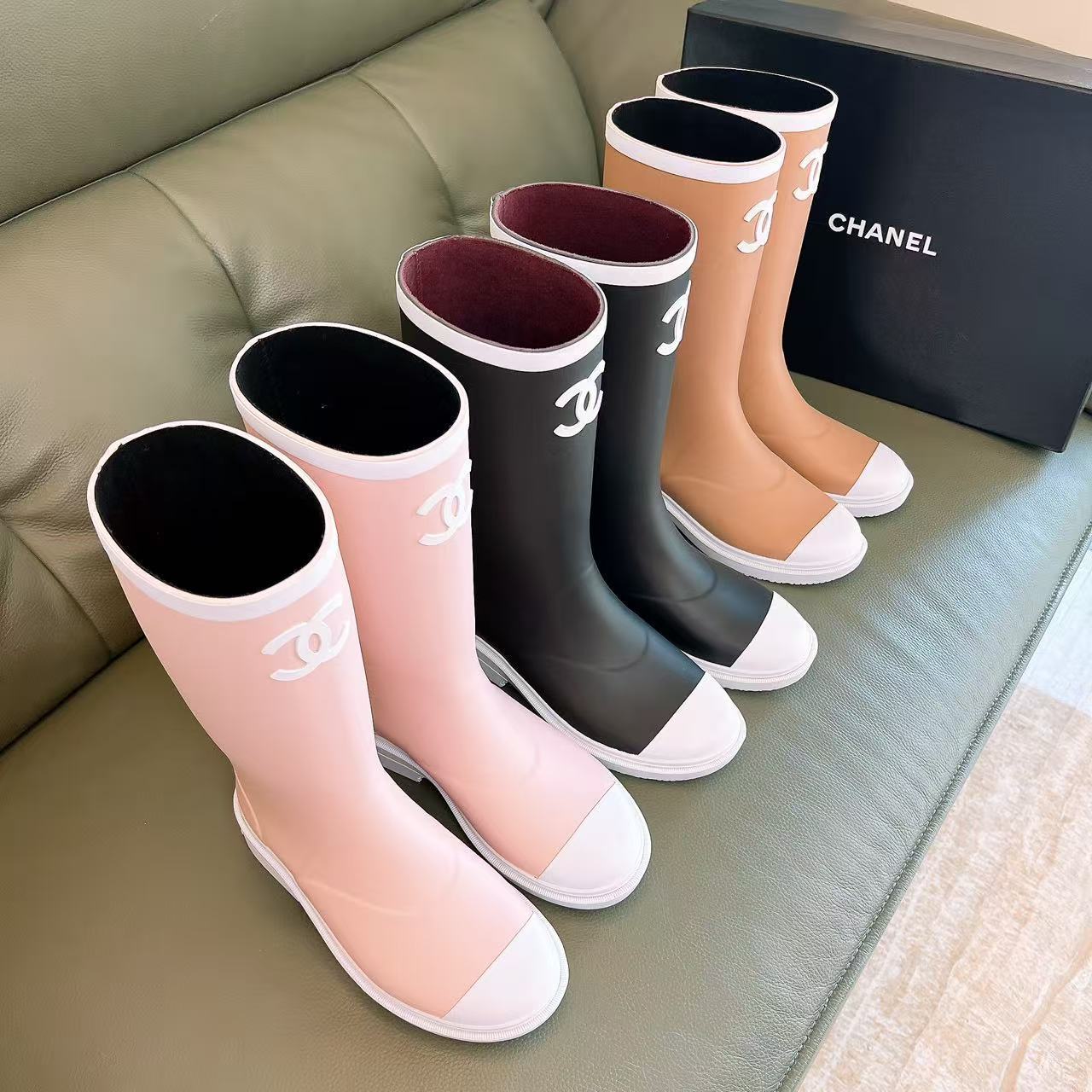 A pair of beige Chanel rain boots with white CC logo and white toe caps placed on a black designer box. - Hình 9