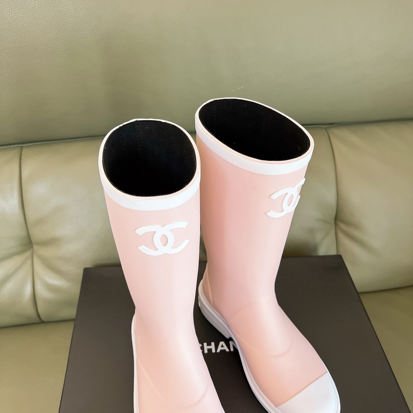 A pair of light pink luxury rubber rain boots with a white interlocking logo and white toe caps placed on a black shoe box. - Hình 7