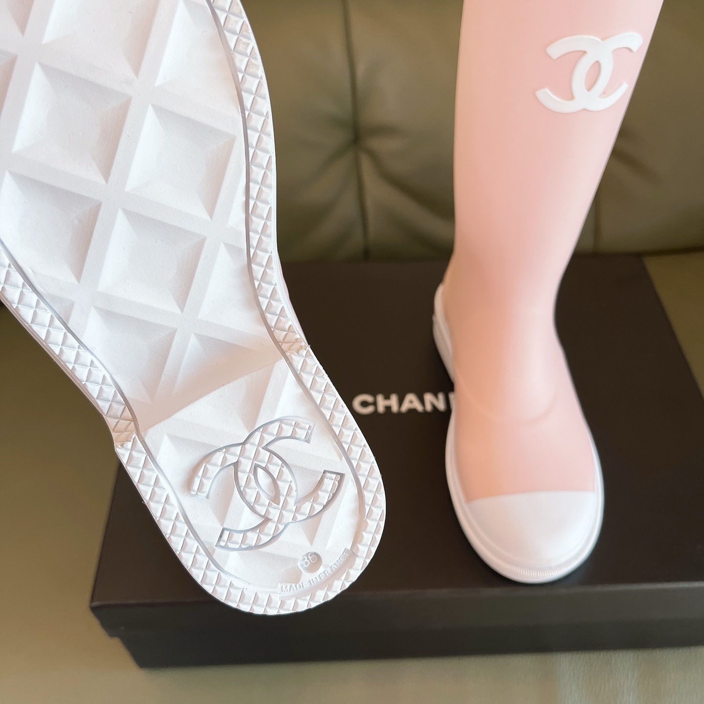A pair of light pink luxury rubber rain boots with a white interlocking logo and white toe caps placed on a black shoe box. - Hình 6