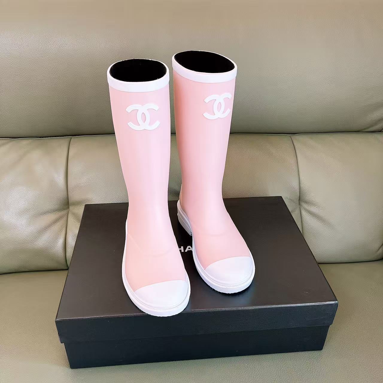 A pair of light pink luxury rubber rain boots with a white interlocking logo and white toe caps placed on a black shoe box. - Hình 5