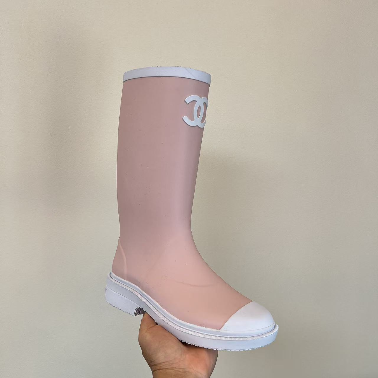 A pair of light pink luxury rubber rain boots with a white interlocking logo and white toe caps placed on a black shoe box. - Hình 3