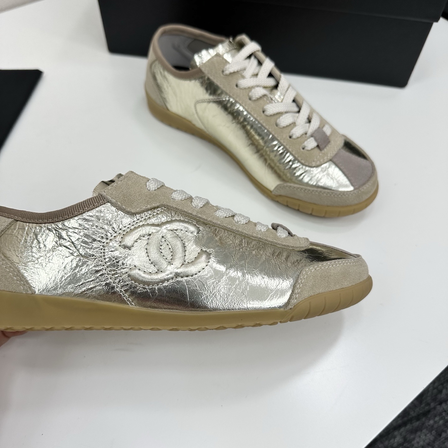 Chanel low-top sneakers featuring metallic gold crinkled leather, beige suede accents, and gum rubber soles displayed on a black box. - Hình 9