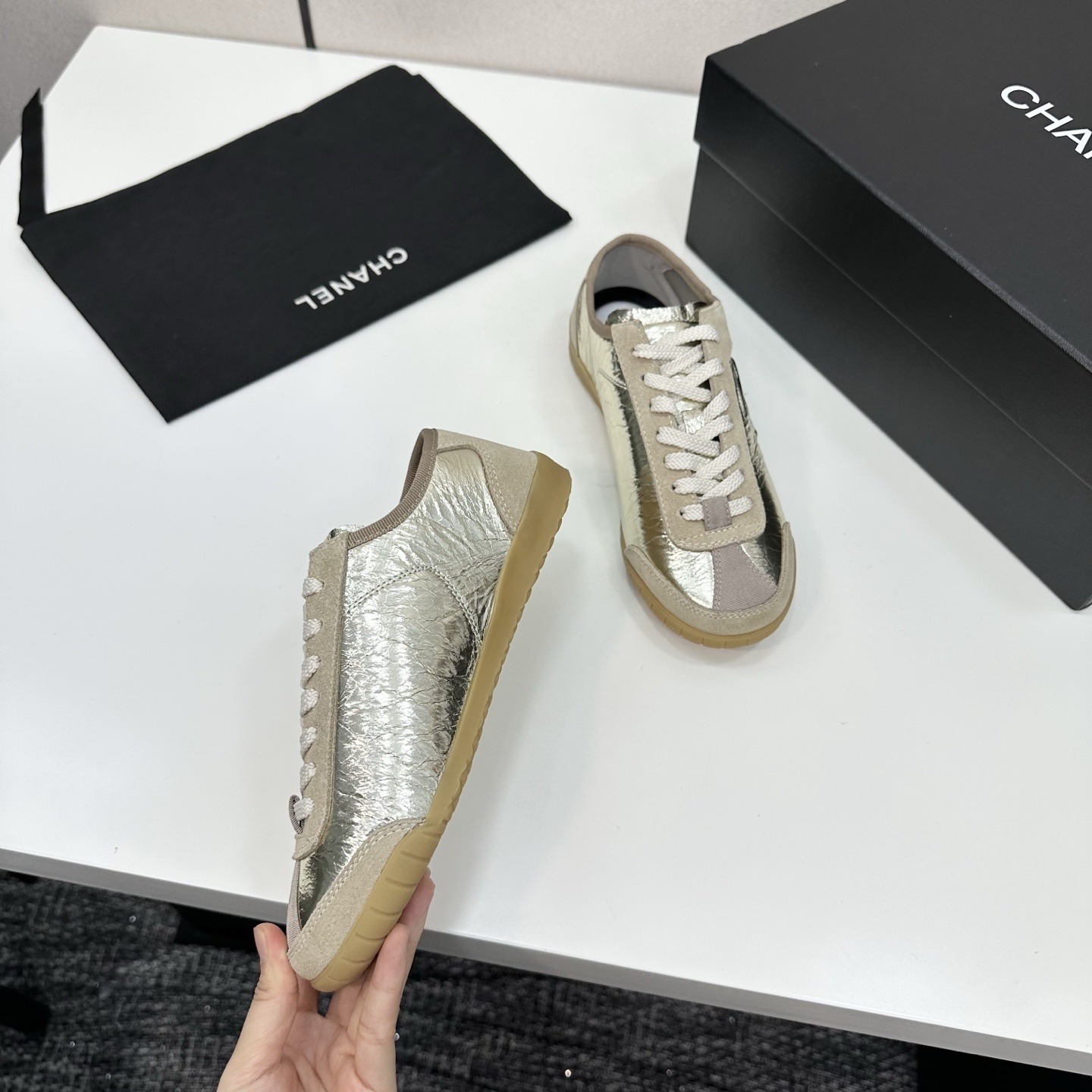 Chanel low-top sneakers featuring metallic gold crinkled leather, beige suede accents, and gum rubber soles displayed on a black box. - Hình 8