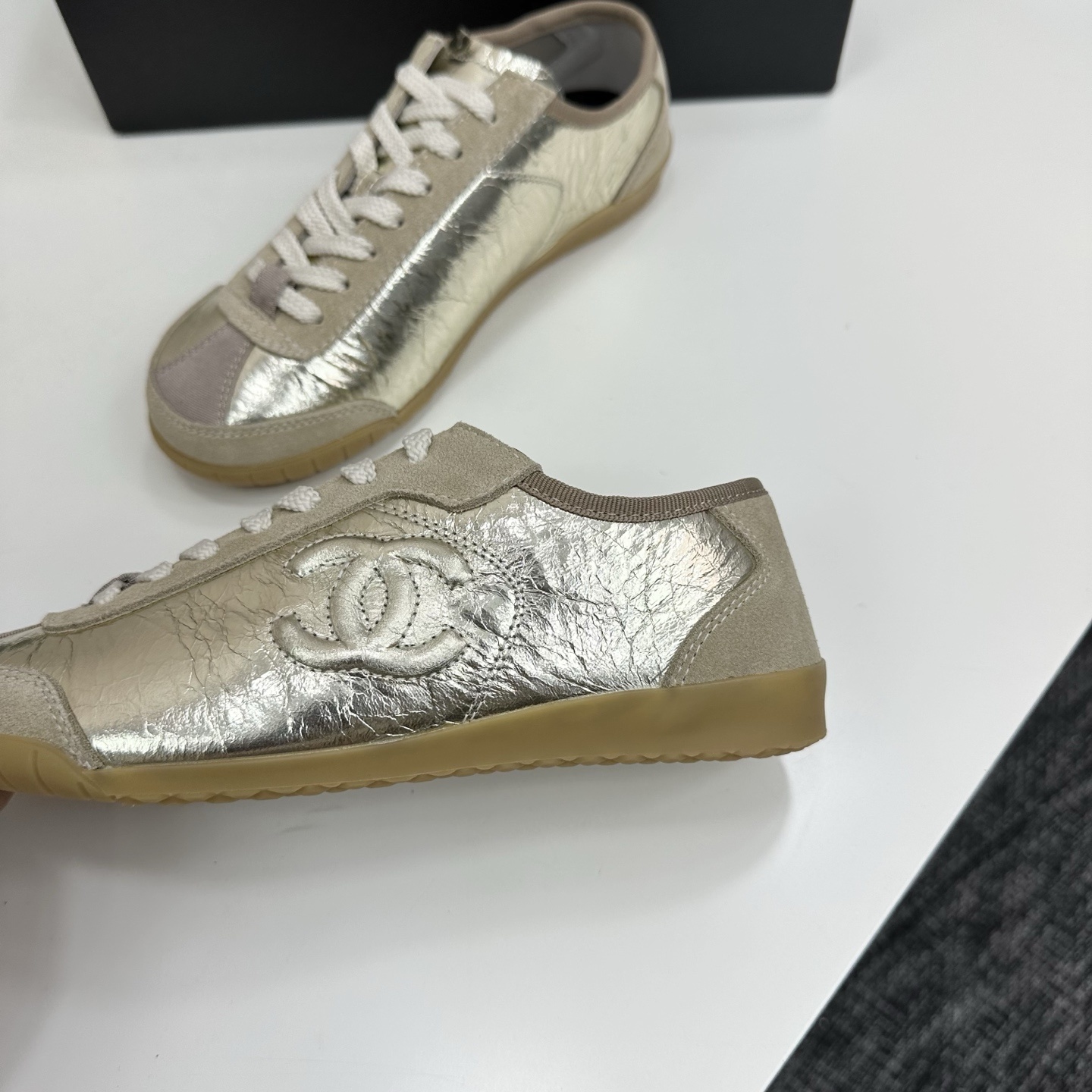 Chanel low-top sneakers featuring metallic gold crinkled leather, beige suede accents, and gum rubber soles displayed on a black box. - Hình 6