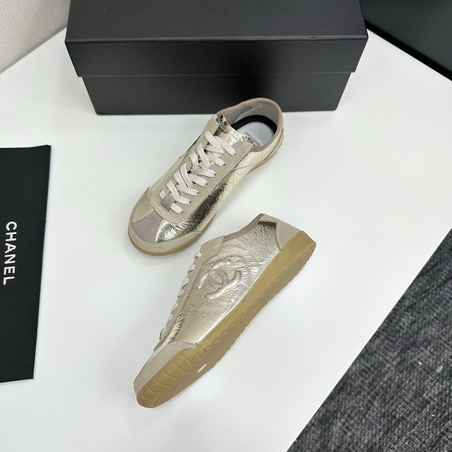 Chanel low-top sneakers featuring metallic gold crinkled leather, beige suede accents, and gum rubber soles displayed on a black box. - Hình 5