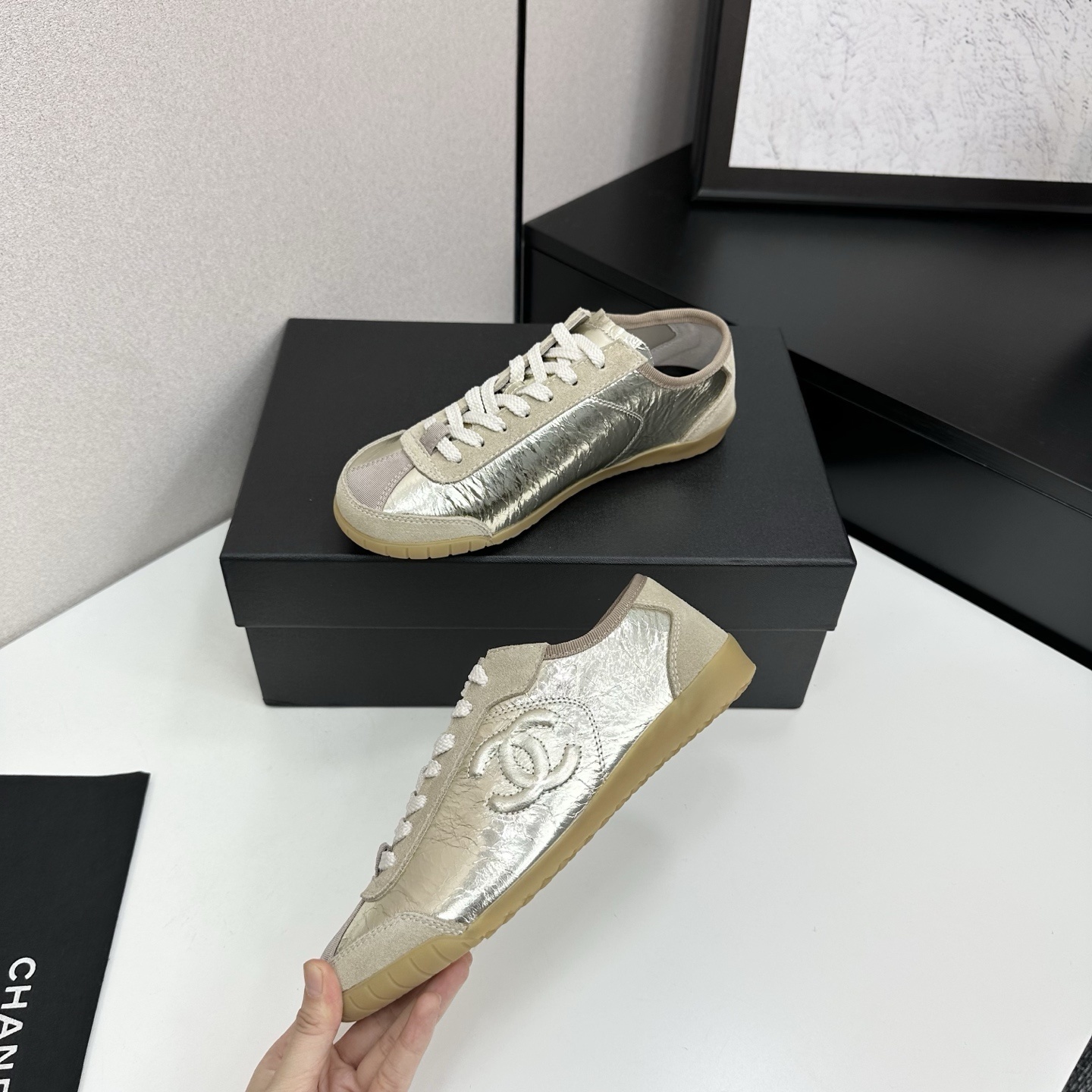 Chanel low-top sneakers featuring metallic gold crinkled leather, beige suede accents, and gum rubber soles displayed on a black box. - Hình 3