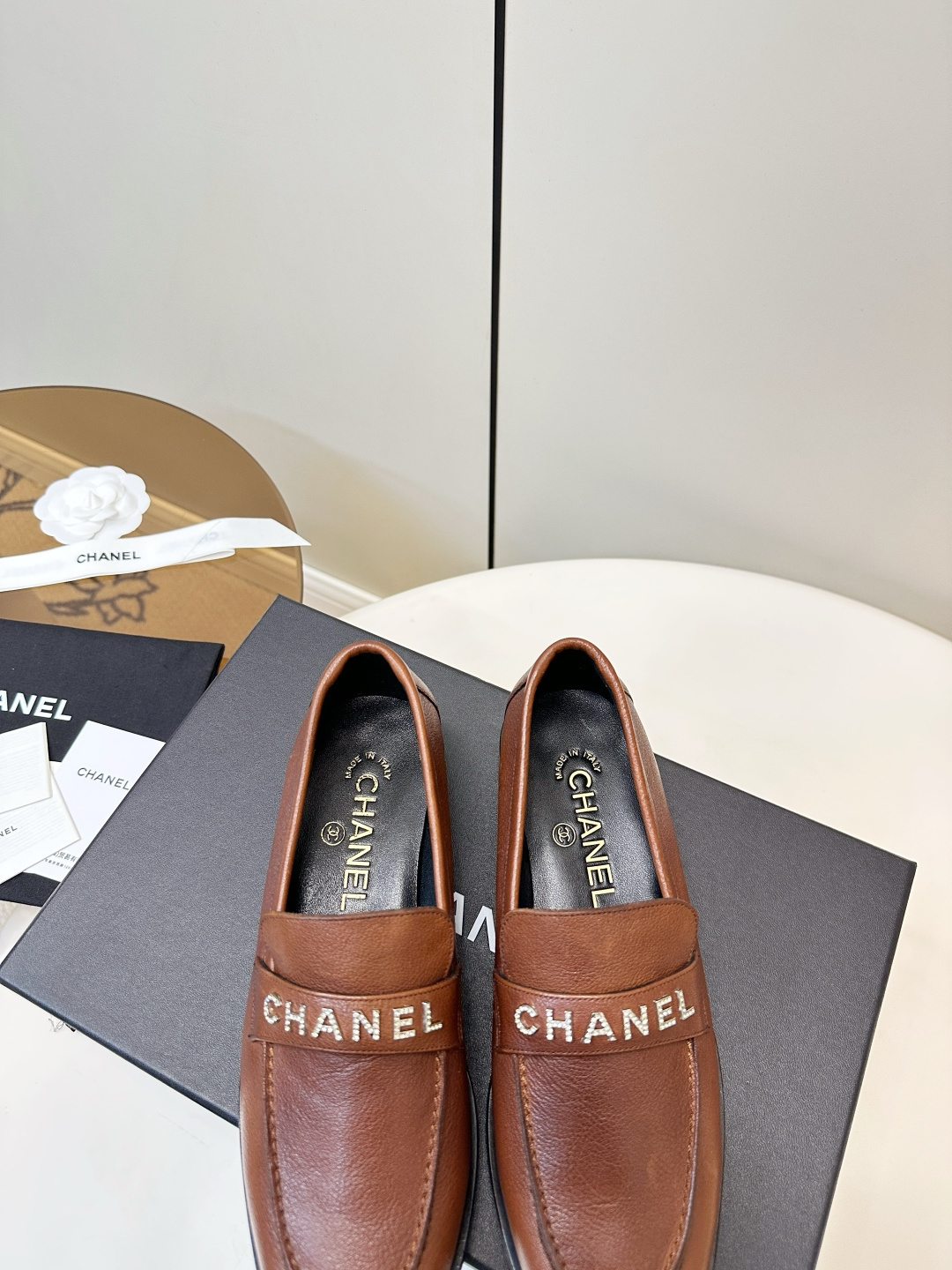 Elegant Chanel brown leather loafers with crystal-embellished logo displayed on a black designer box. - Hình 9