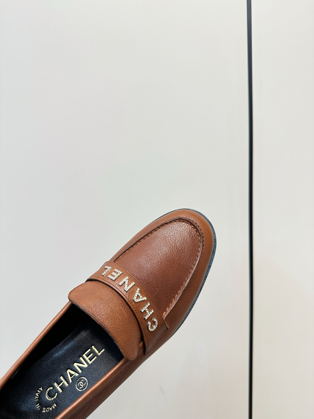 Elegant Chanel brown leather loafers with crystal-embellished logo displayed on a black designer box. - Hình 8