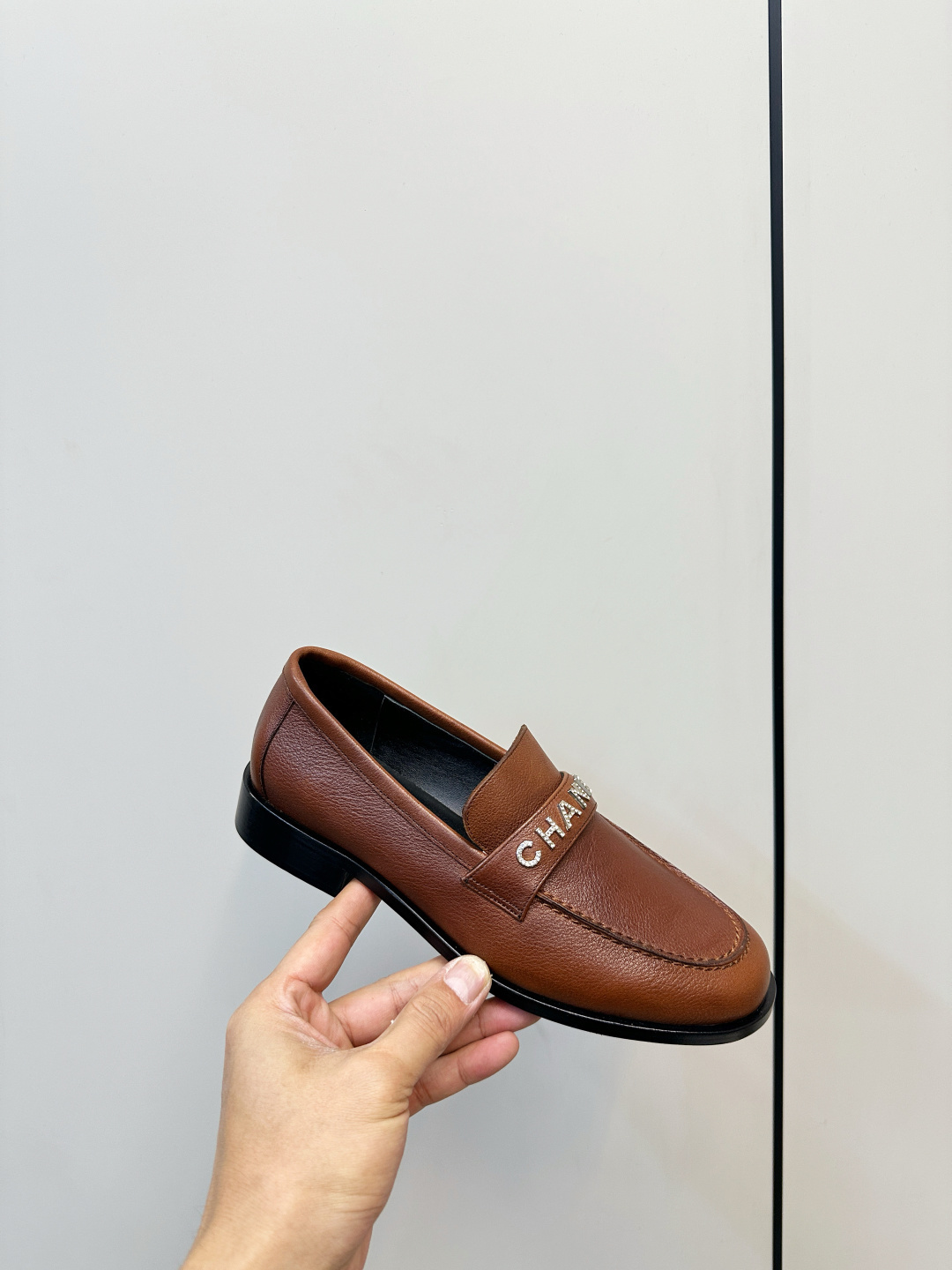 Elegant Chanel brown leather loafers with crystal-embellished logo displayed on a black designer box. - Hình 7