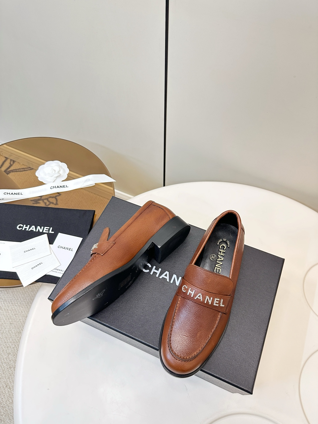 Elegant Chanel brown leather loafers with crystal-embellished logo displayed on a black designer box. - Hình 6