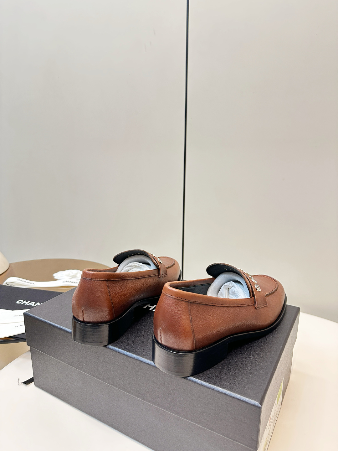 Elegant Chanel brown leather loafers with crystal-embellished logo displayed on a black designer box. - Hình 5