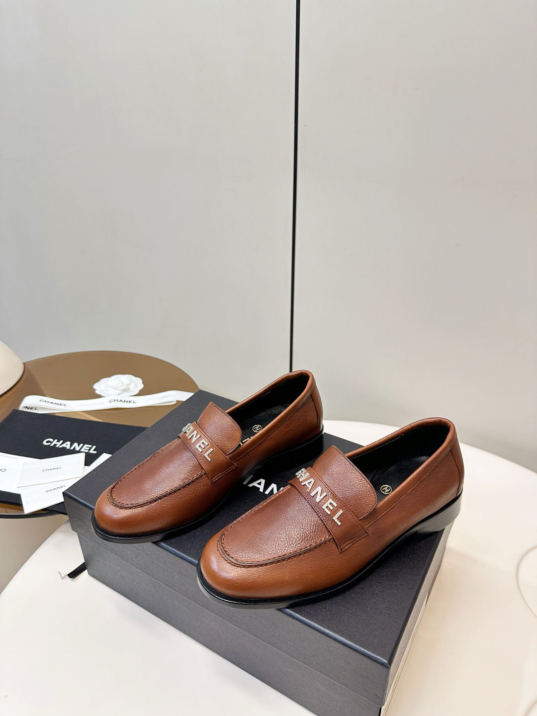 Elegant Chanel brown leather loafers with crystal-embellished logo displayed on a black designer box. - Hình 4