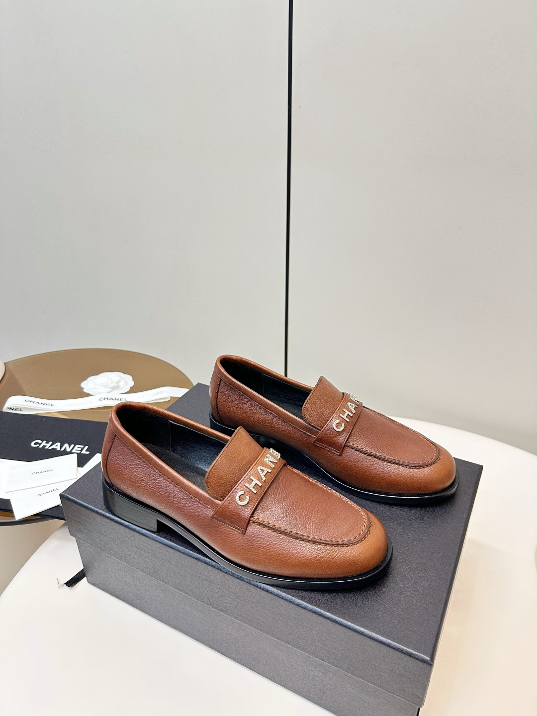 Elegant Chanel brown leather loafers with crystal-embellished logo displayed on a black designer box. - Hình 3