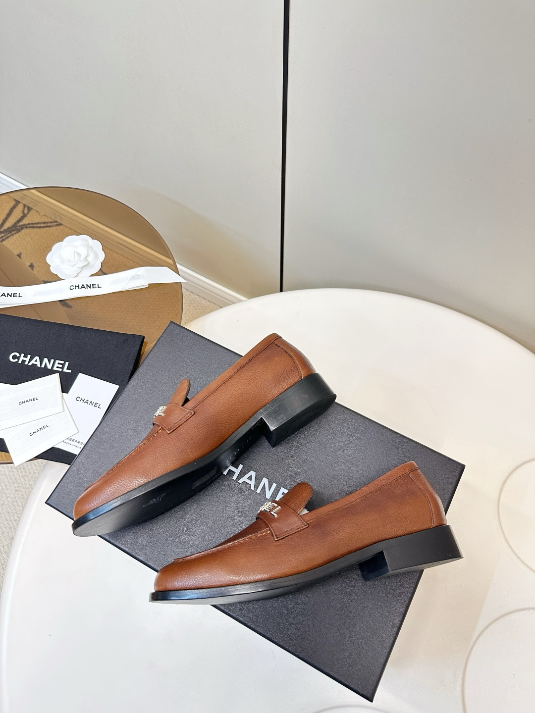 Elegant Chanel brown leather loafers with crystal-embellished logo displayed on a black designer box. - Hình 2
