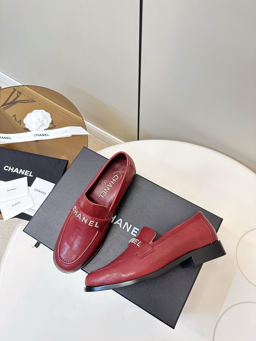 A pair of burgundy red leather Chanel loafers with crystal logo lettering on a black designer box. - Hình 9