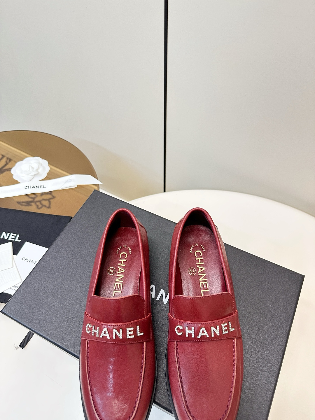 A pair of burgundy red leather Chanel loafers with crystal logo lettering on a black designer box. - Hình 8