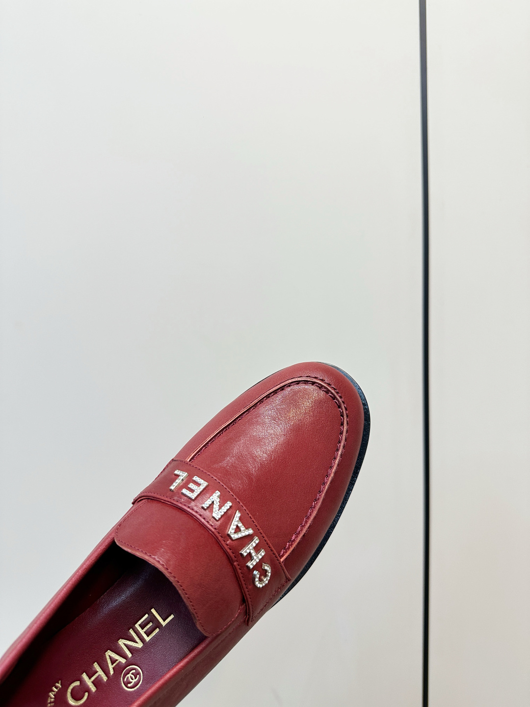 A pair of burgundy red leather Chanel loafers with crystal logo lettering on a black designer box. - Hình 7