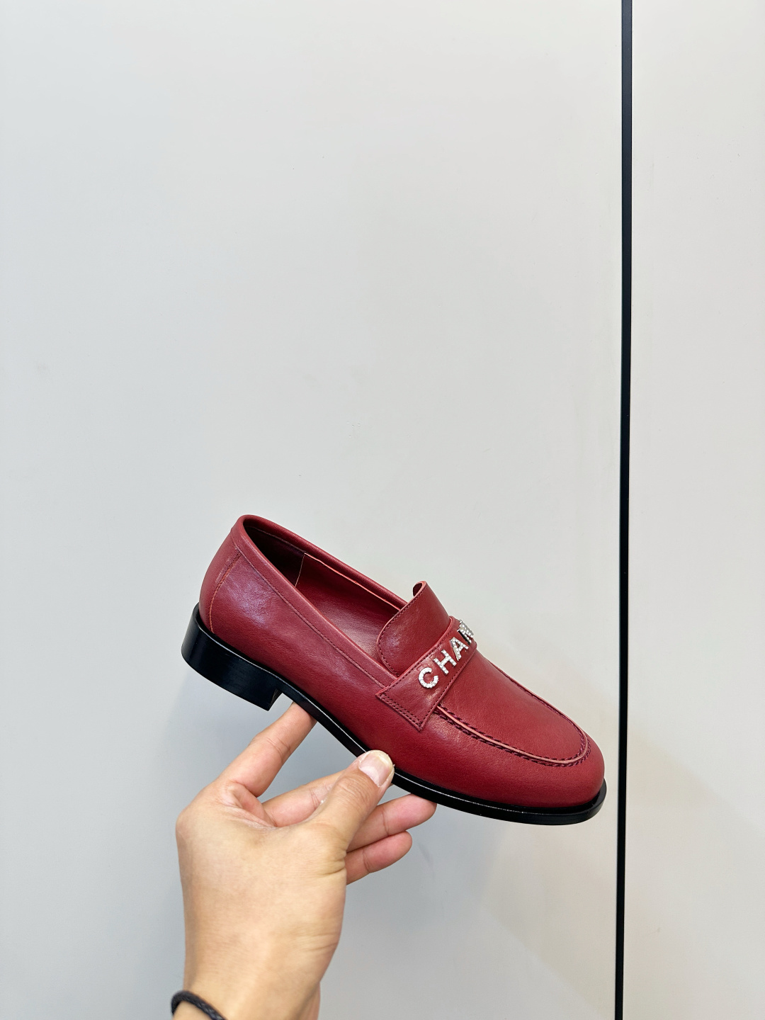 A pair of burgundy red leather Chanel loafers with crystal logo lettering on a black designer box. - Hình 6