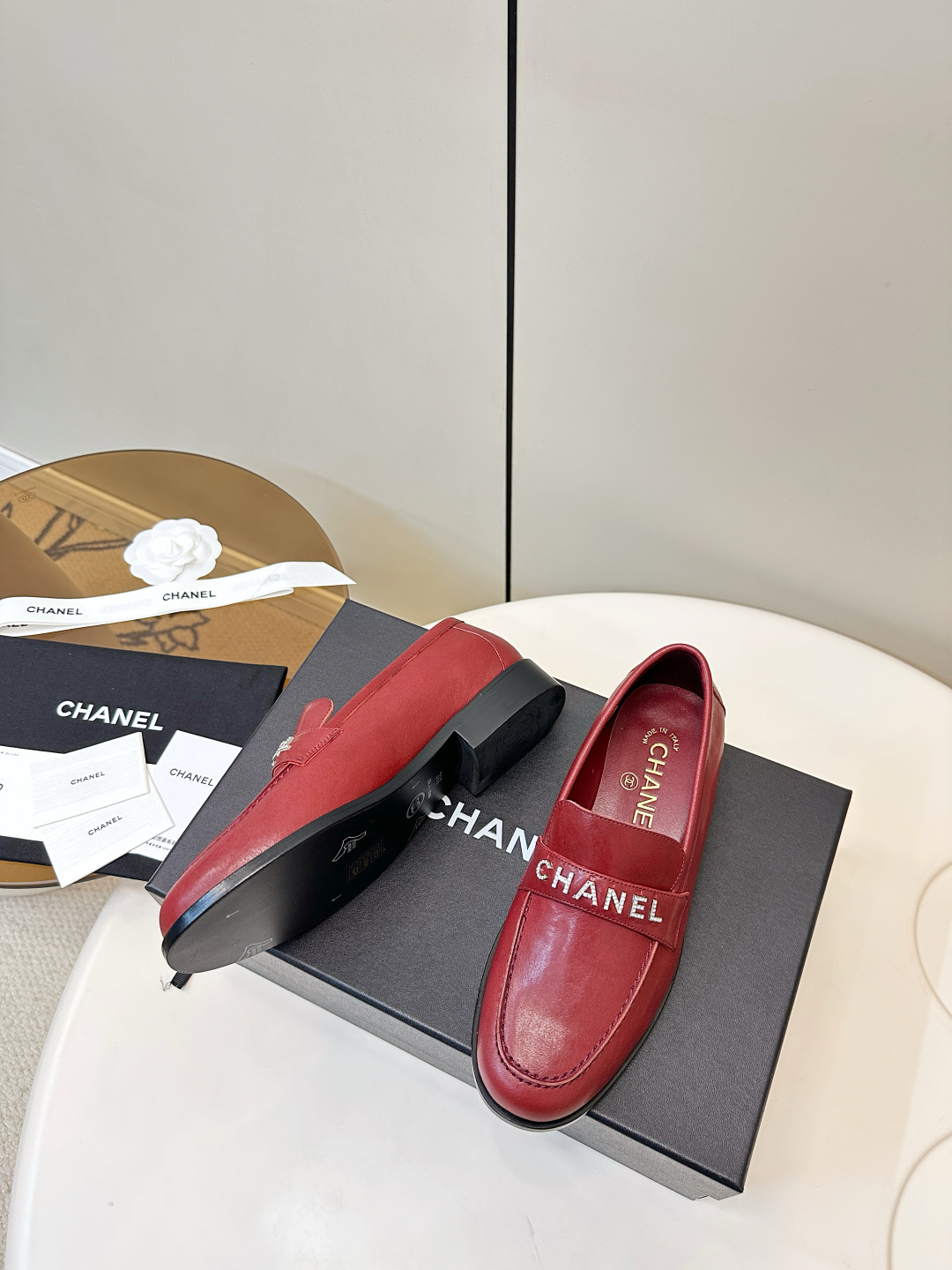 A pair of burgundy red leather Chanel loafers with crystal logo lettering on a black designer box. - Hình 5