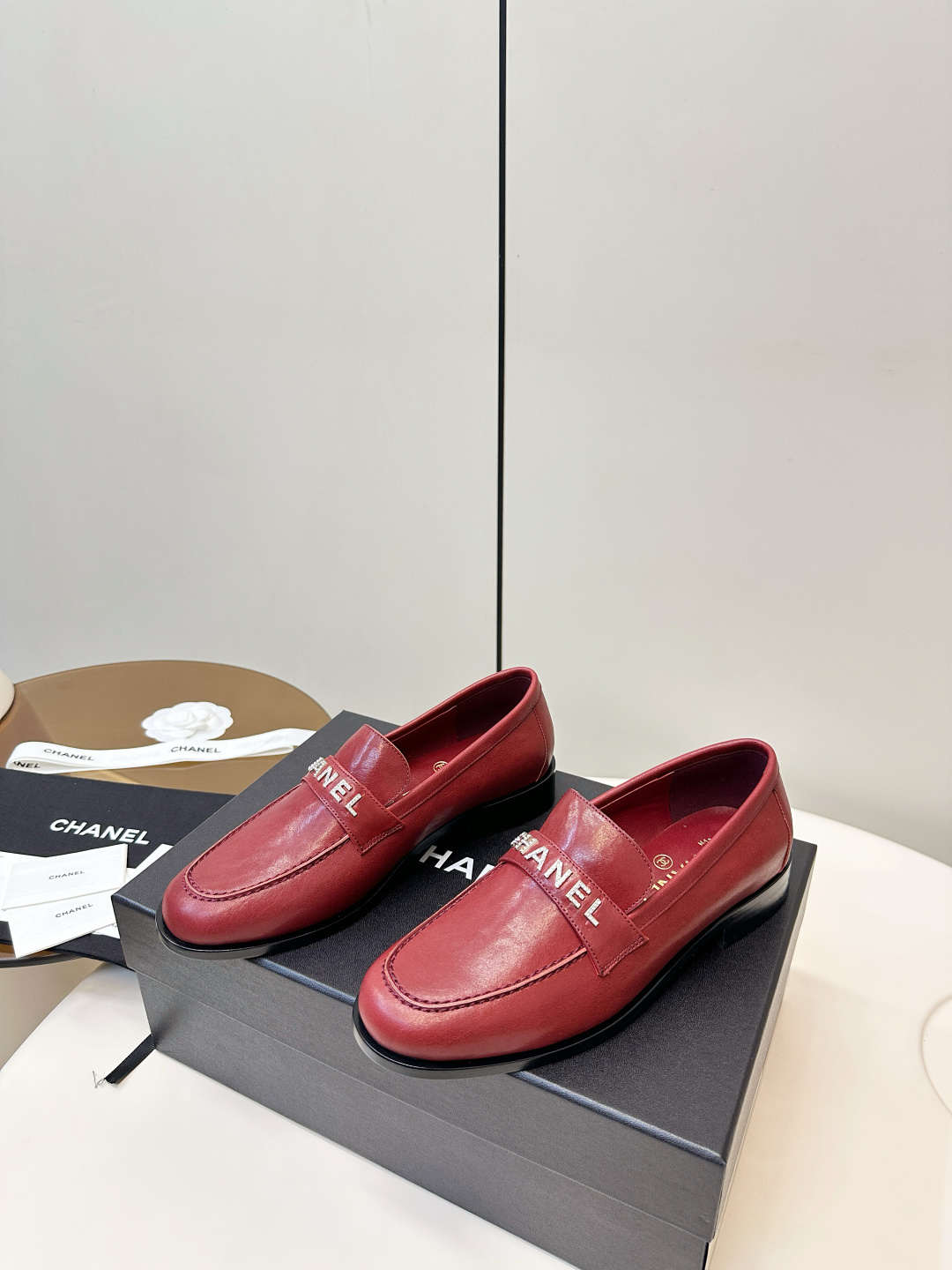 A pair of burgundy red leather Chanel loafers with crystal logo lettering on a black designer box. - Hình 3