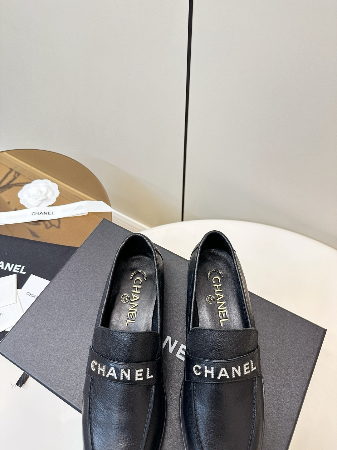 A pair of black Chanel leather loafers with silver crystal logo embellishment displayed on a black box. - Hình 8